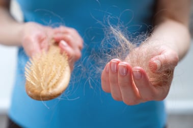 A woman holds a wooden comb in her hands, cleans it of fallen hair after combing, a side effect of chemotherapy and radiation for cancer.