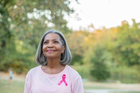 A middle-aged woman wears a pink breast cancer awareness ribbon